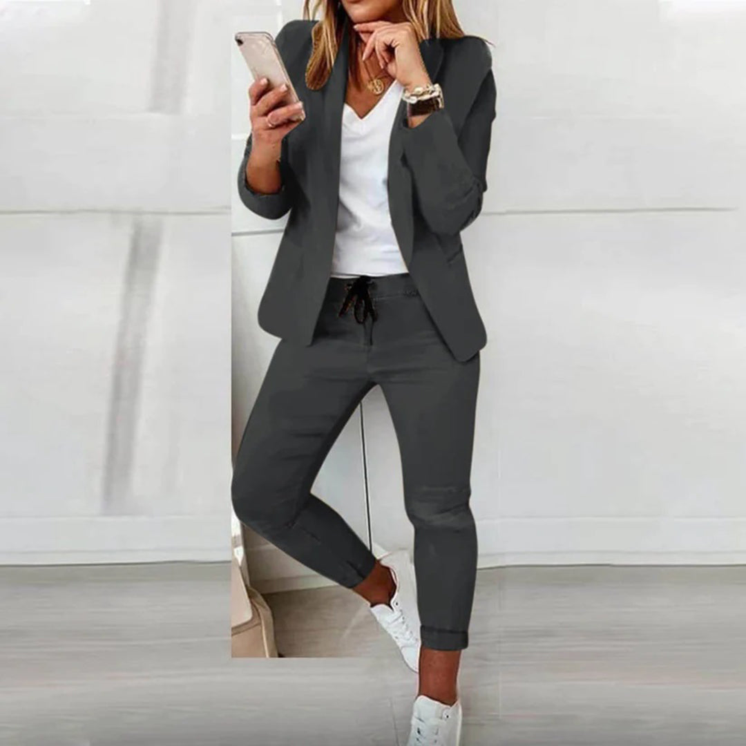 A woman wearing a casual blazer paired with jogger pants, standing comfortably in a relaxed pose against a neutral background. 3