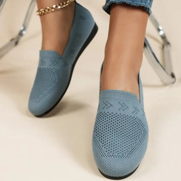 A pair of women's slip-on sneakers featuring a breathable upper design and a lightweight sole, displayed against a neutral background. 1