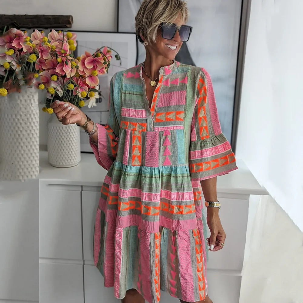 A woman wearing a boho-style mini dress with ruffles, standing outdoors in a natural setting. 0