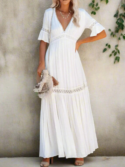 A woman wearing a long, lace maxi dress with a V-neckline and short sleeves, standing outdoors at a wedding event. 0