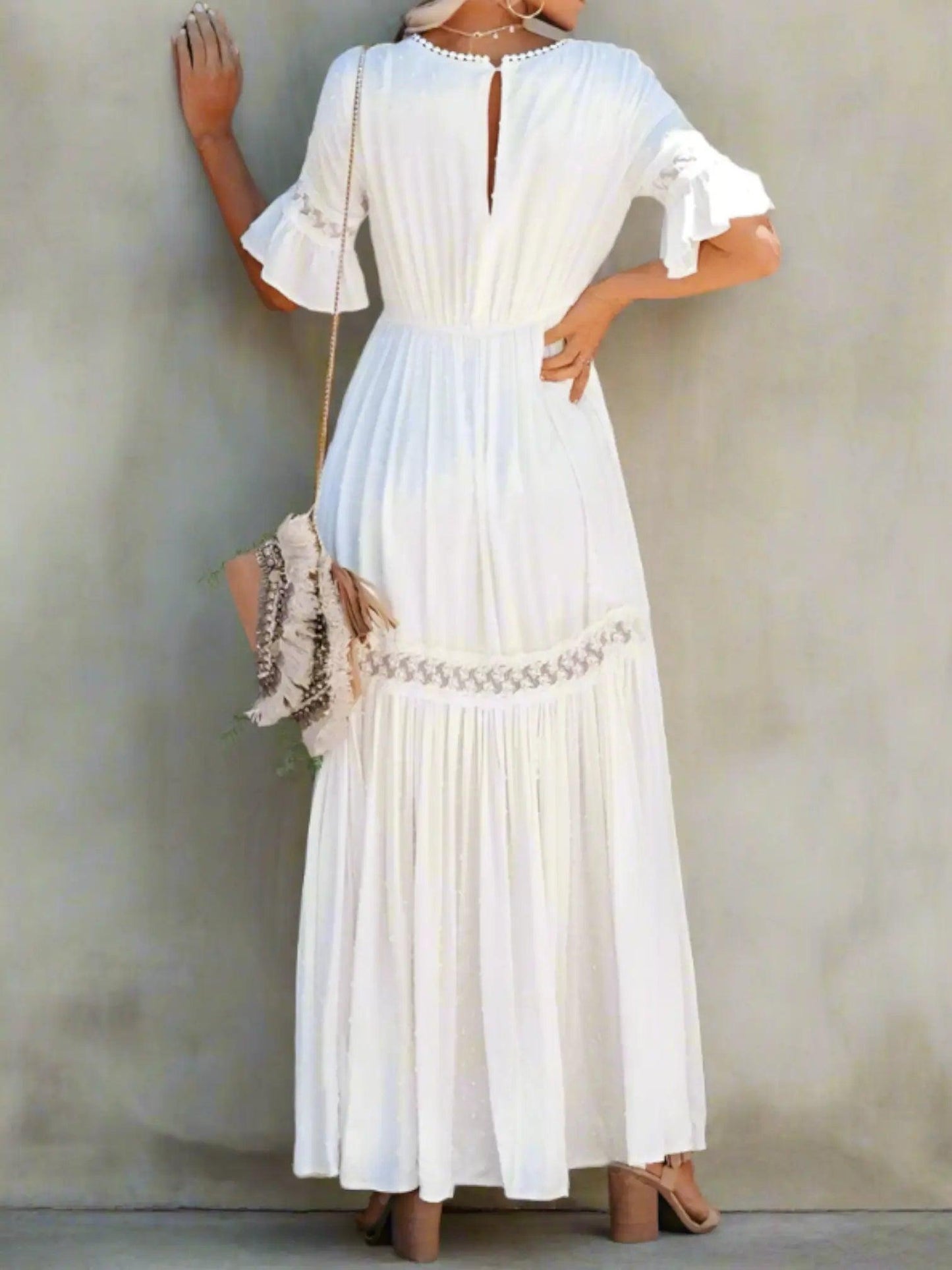 A woman wearing a long, lace maxi dress with a V-neckline and short sleeves, standing outdoors at a wedding event. 1