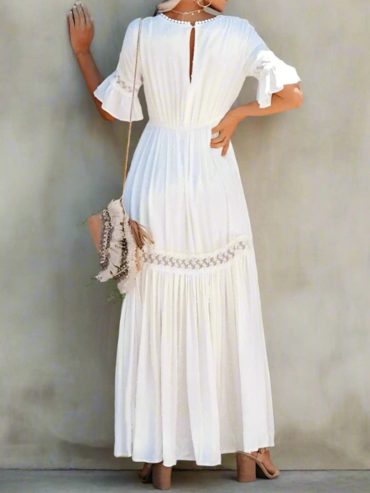 A woman wearing a long, lace maxi dress with a V-neckline and short sleeves, standing outdoors at a wedding event. 1