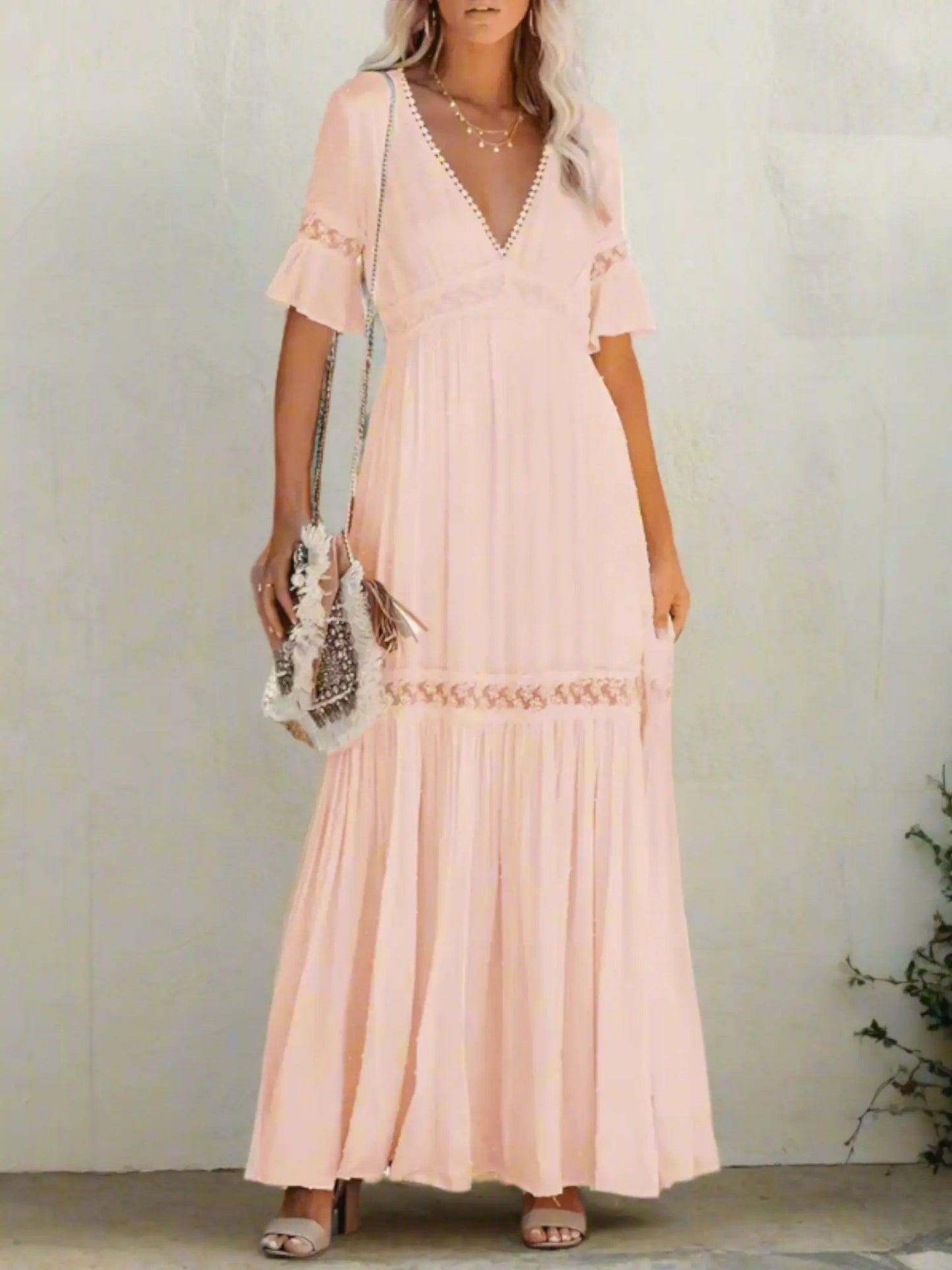 A woman wearing a long, lace maxi dress with a V-neckline and short sleeves, standing outdoors at a wedding event. 2