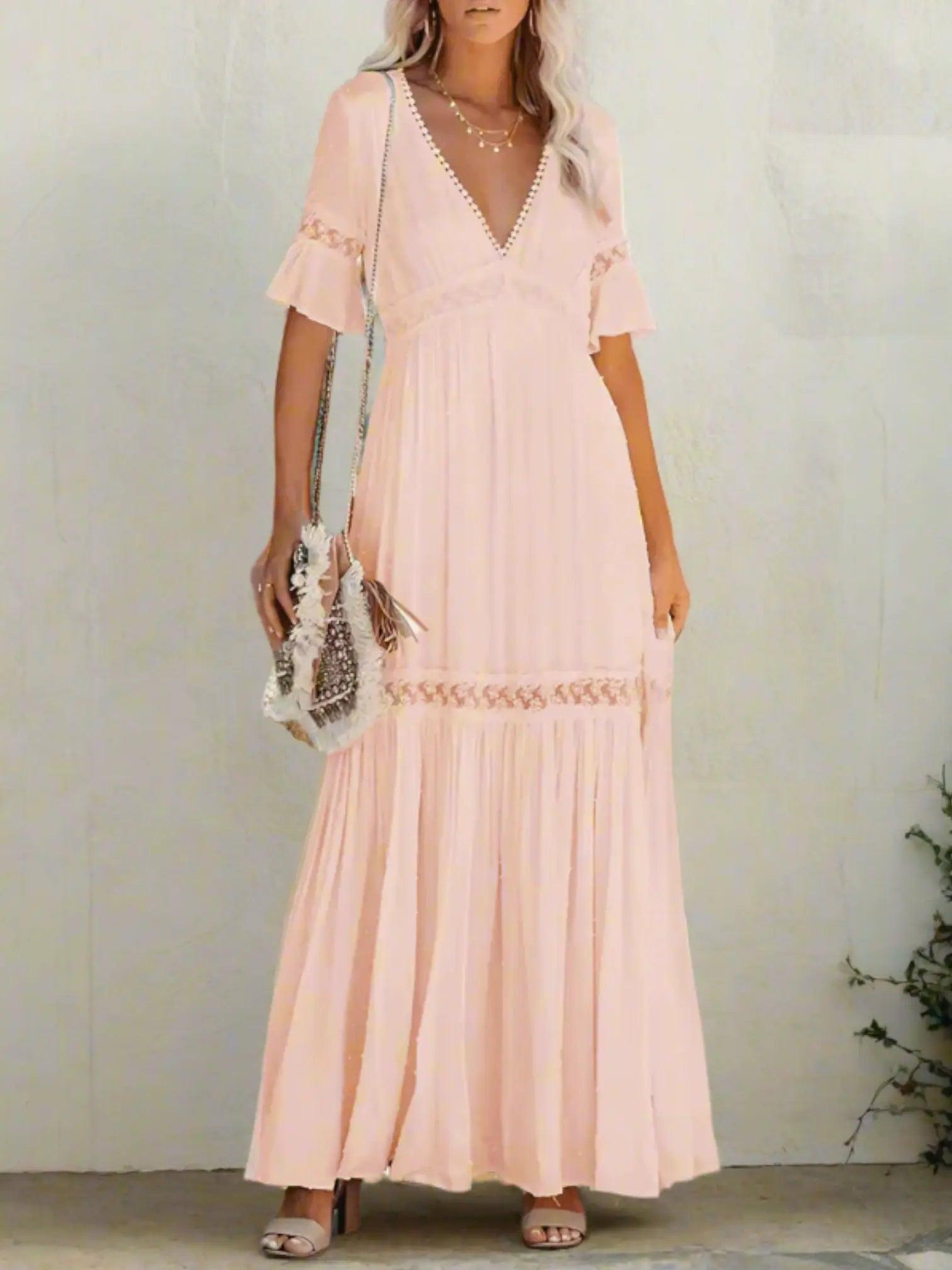 A woman wearing a long, lace maxi dress with a V-neckline and short sleeves, standing outdoors at a wedding event. 2