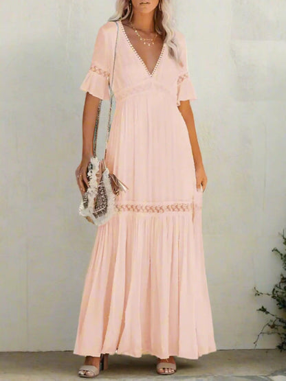 A woman wearing a long, lace maxi dress with a V-neckline and short sleeves, standing outdoors at a wedding event. 2